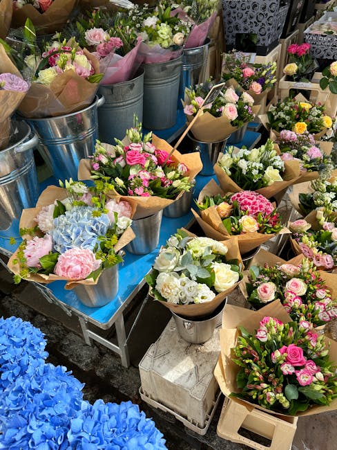 A vibrant display of freshly arranged flower bouquets at Wood Green High Road markets, featuring a variety of colorful blooms including pink roses, white roses, blue hydrangeas, and various smaller fl
